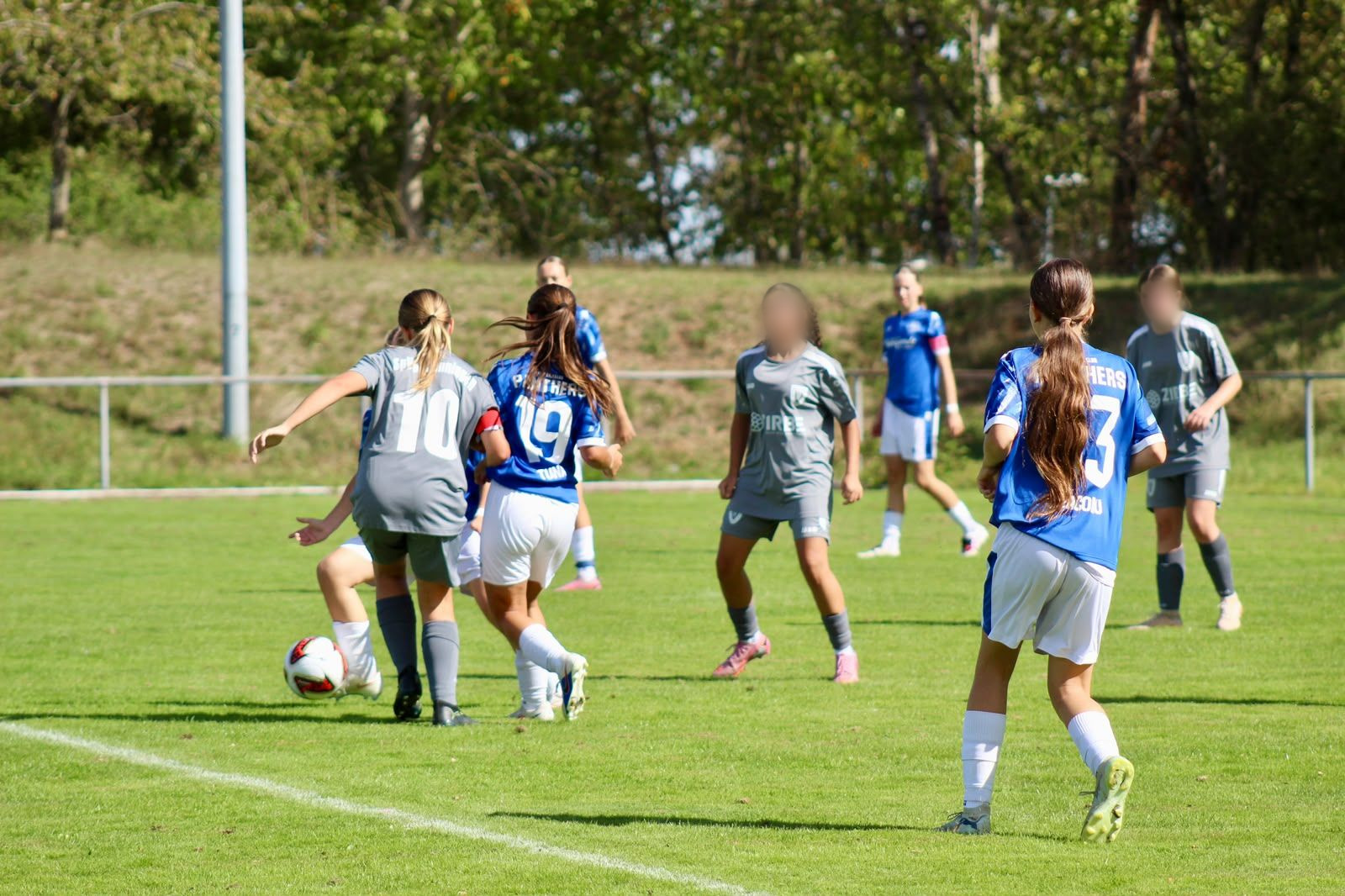 Mehrere Spielerinnen beider Teams im Mittelfeld, eine Spielerin des FC Panthers mit der Rückennummer 19 im Zweikampf mit einer Gegenspielerin in Grau.