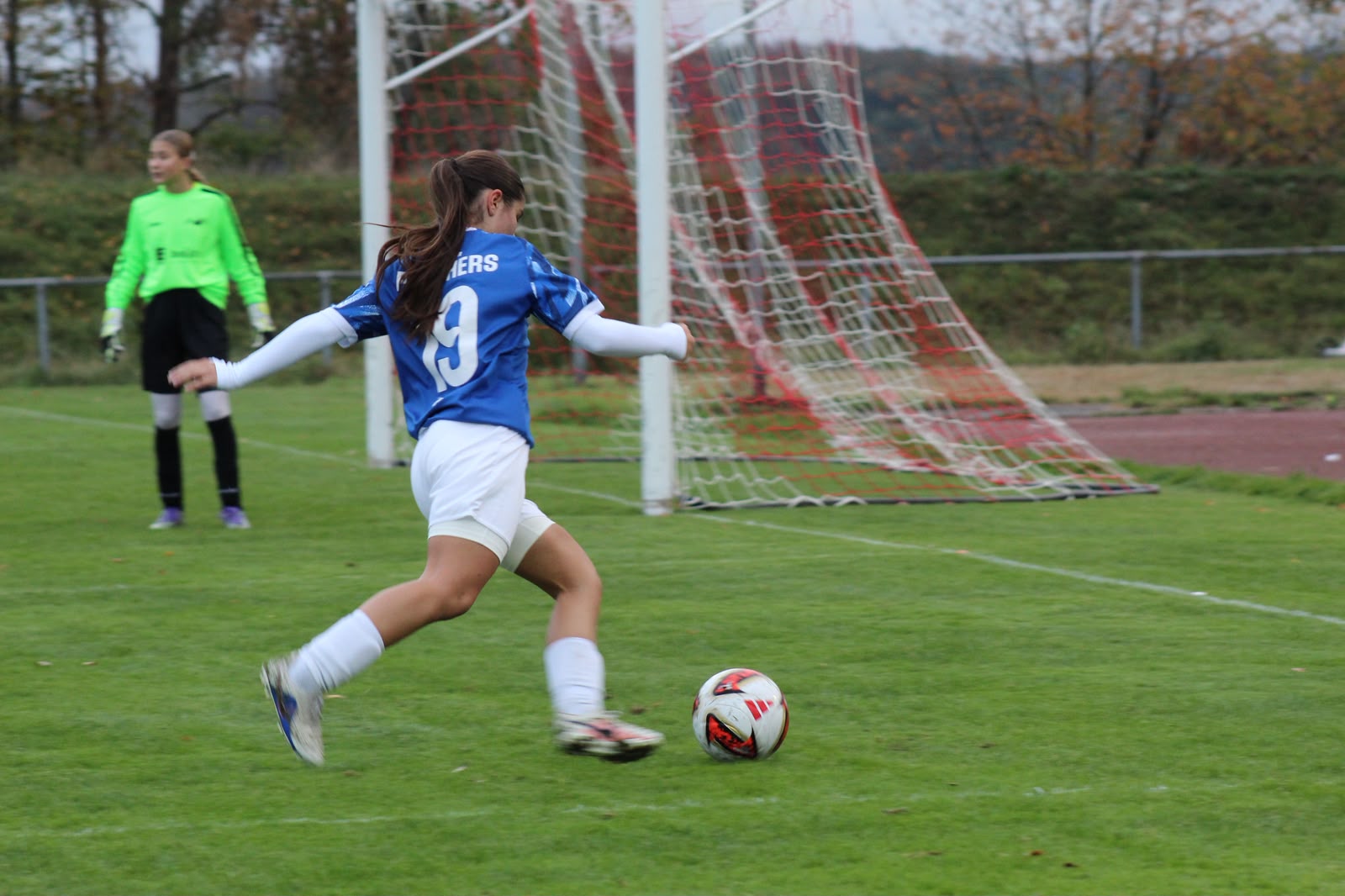 Spielerin mit der Rückennummer 19 im blauen Panthers-Trikot holt nahe dem gegnerischen Tor zum Schuss aus, links die Torhüterin in Neongrün.