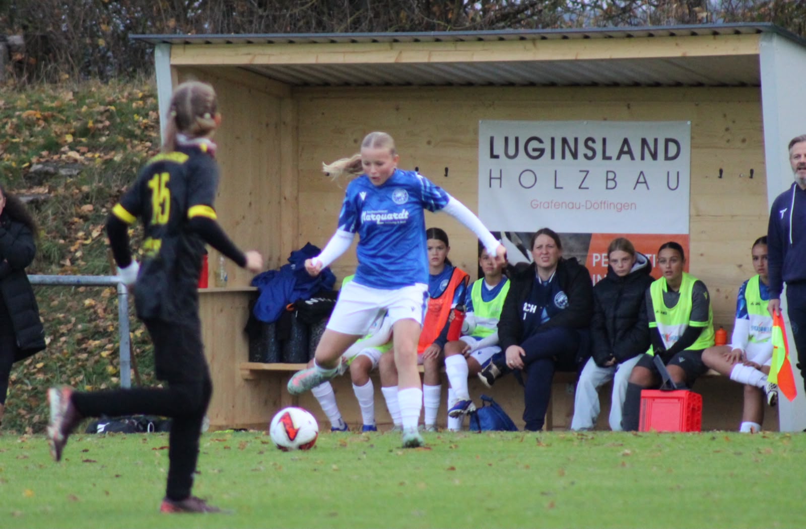 Panthers-Spielerin führt den Ball an der Seitenlinie vor der Ersatzbank, auf der Auswechselspielerinnen und Betreuerinnen sitzen.