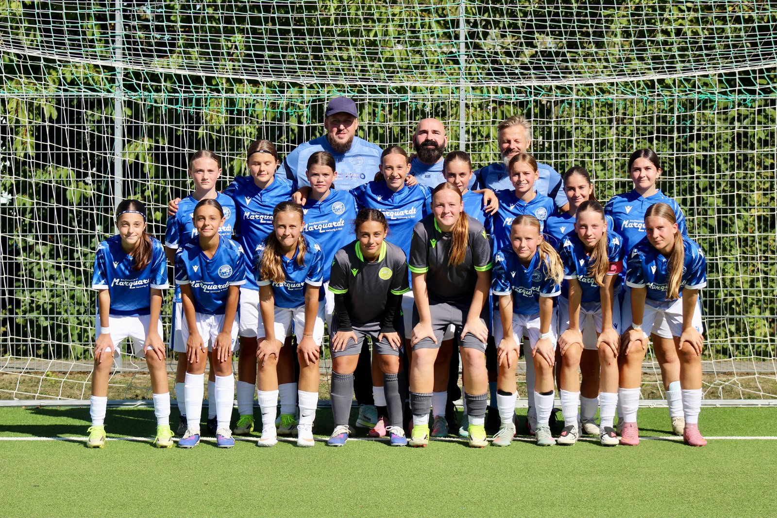 Mannschaftsfoto der U15 des FC Panthers mit Spielerinnen in blauen Trikots, zwei Torhüterinnen in Grau und drei Betreuern vor einem Tor.