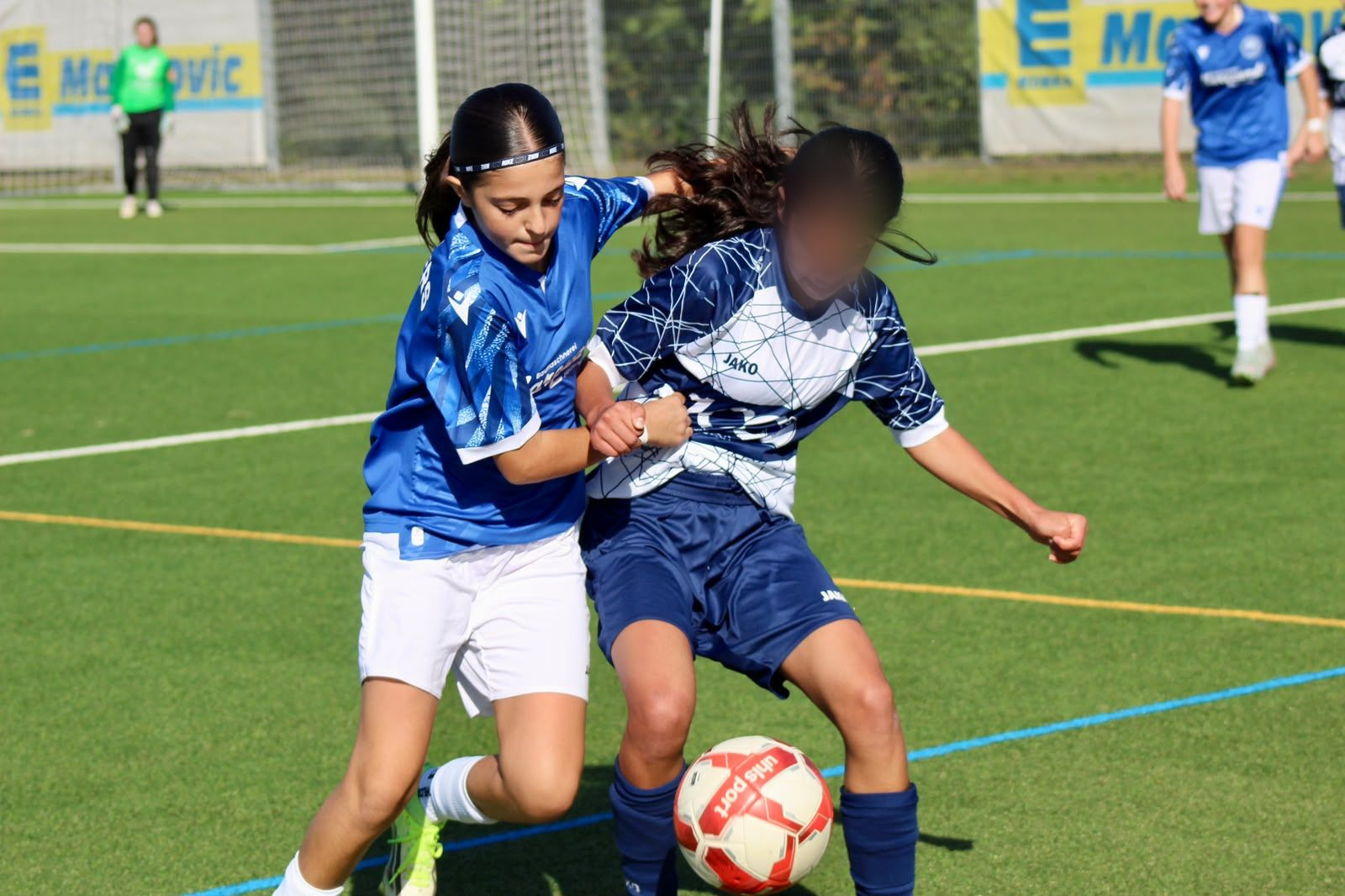 Zweikampf um den Ball zwischen einer Spielerin des FC Panthers in Blau und einer Gegenspielerin in Weiß-Dunkelblau auf Kunstrasen.