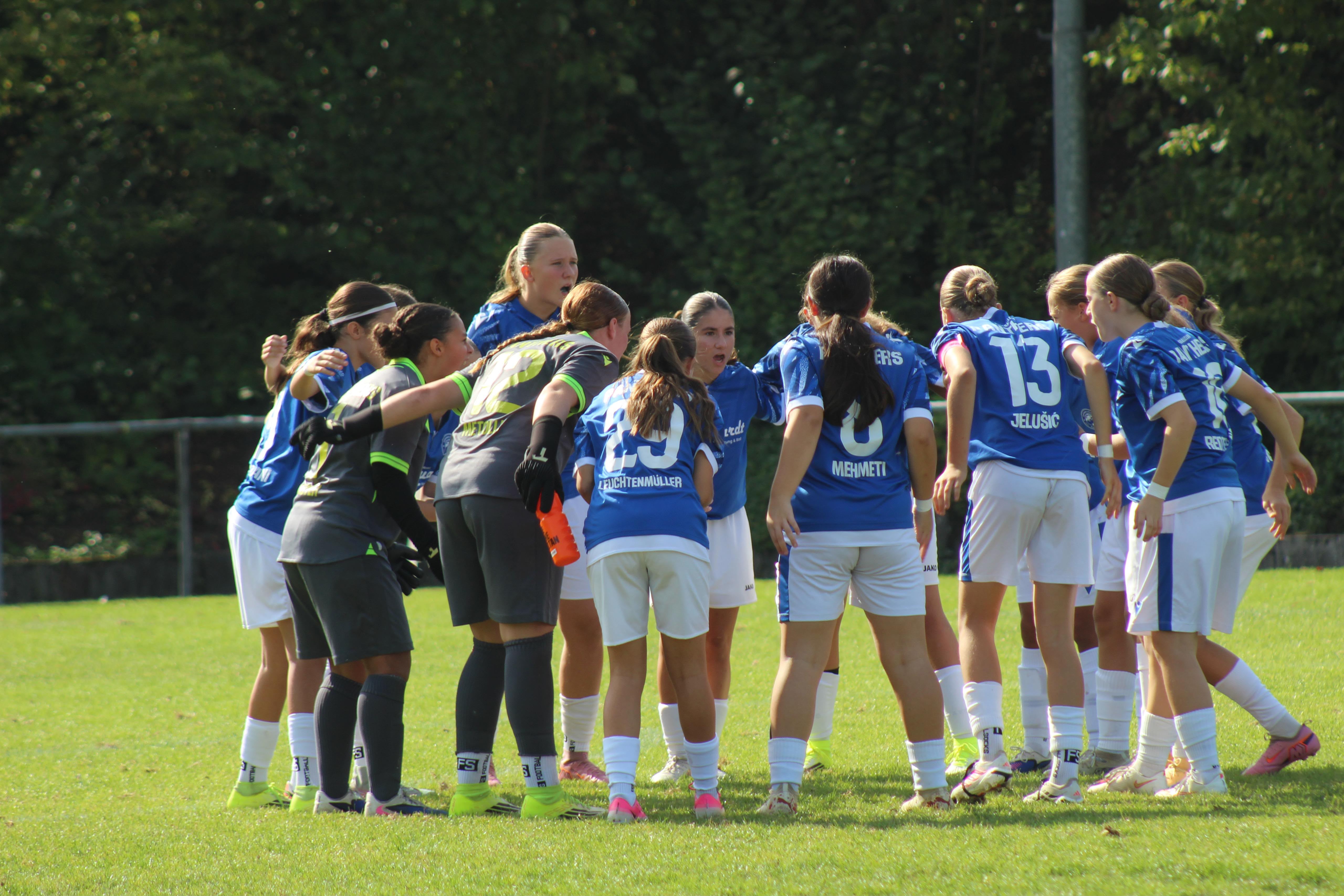 Feldspielerinnen und Torhüterinnen des FC Panthers stehen auf dem Rasen im Kreis zusammen